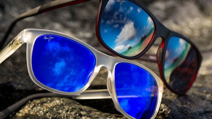 2 pairs of sunglasses displayed on rock with sky reflection on lenses