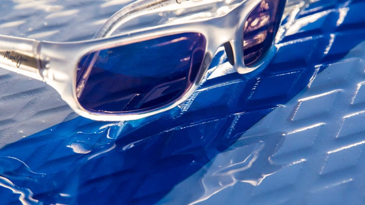 crystal frame sunglasses with blue lenses displayed on wet rubber textured surface