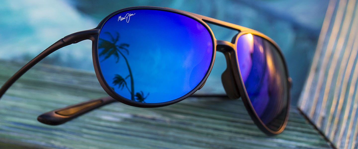 matte black sunglass frame with blue lenses reflecting the sky and palm trees